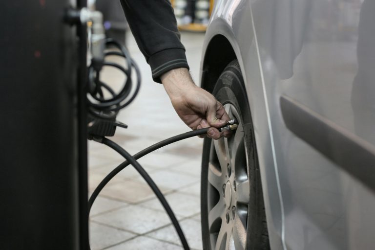 Mechanic inflating a car tire inside an auto repair shop, ensuring optimal tire pressure.